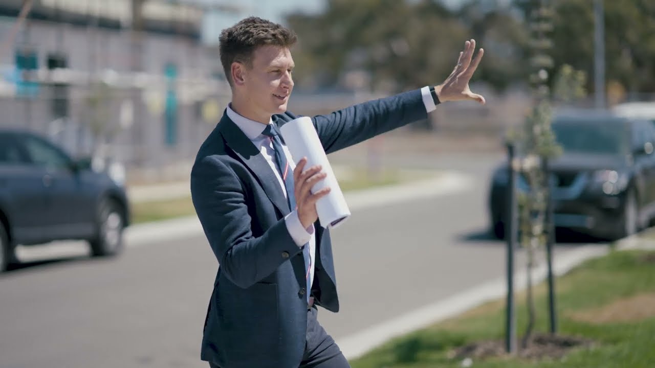 Ben Williams calling an auction on a suburban street, arm raised, contract rolled in one hand